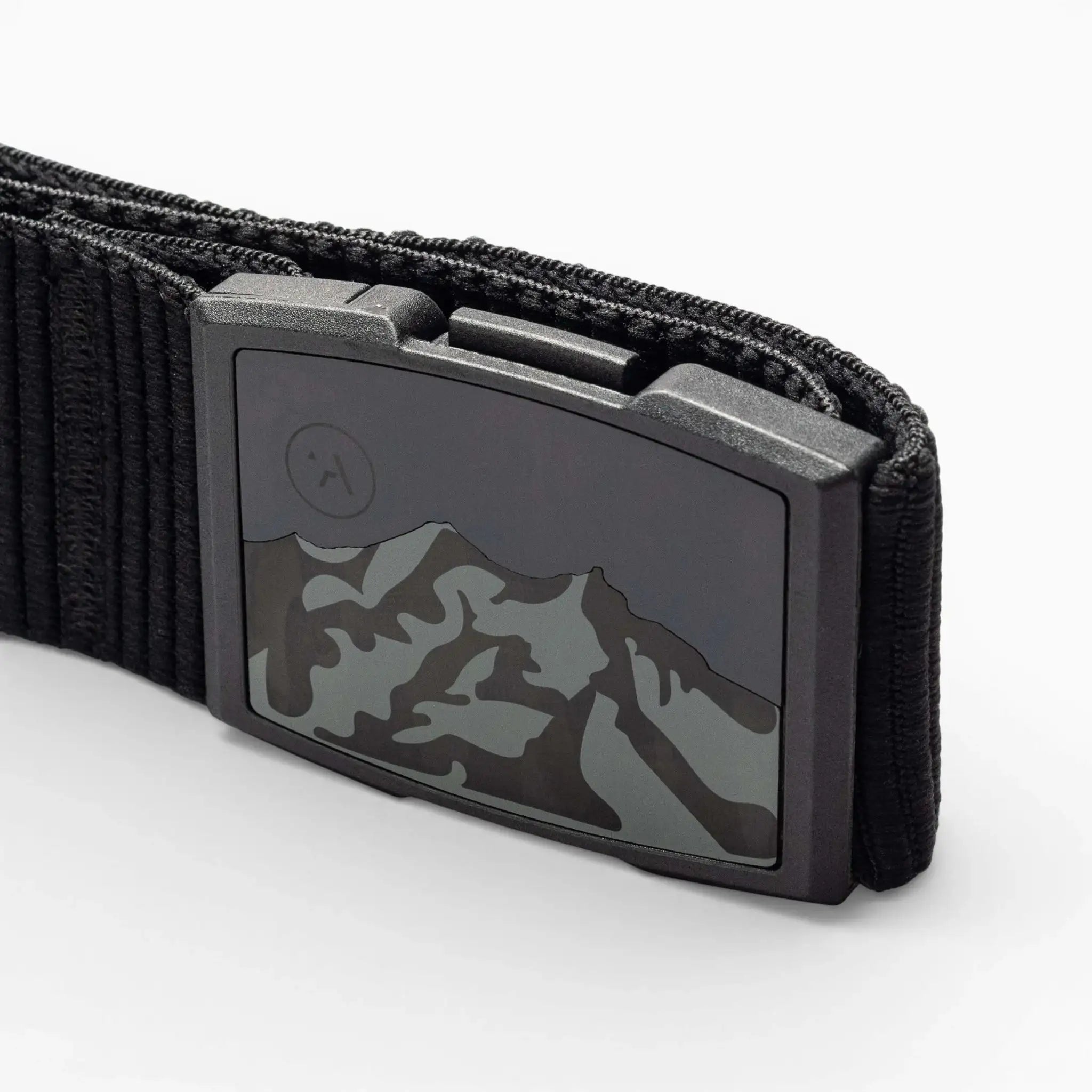 Close-up of the Arcade Belts Woody elastic stretch belt with a metal buckle featuring a mountain range design and an etched moon or sun in the corner. The white background highlights this low-profile belt.