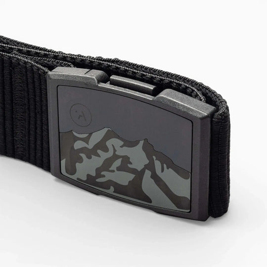 Close-up of the Arcade Belts Woody elastic stretch belt with a metal buckle featuring a mountain range design and an etched moon or sun in the corner. The white background highlights this low-profile belt.