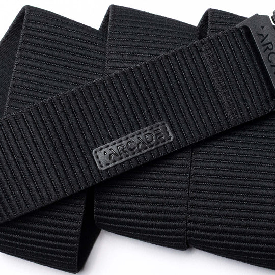 A close-up of the black, ribbed woven Woody belt by Arcade Belts features a rectangular patch with ARCADE in raised letters, showcasing its durable stitching and elastic stretch design.