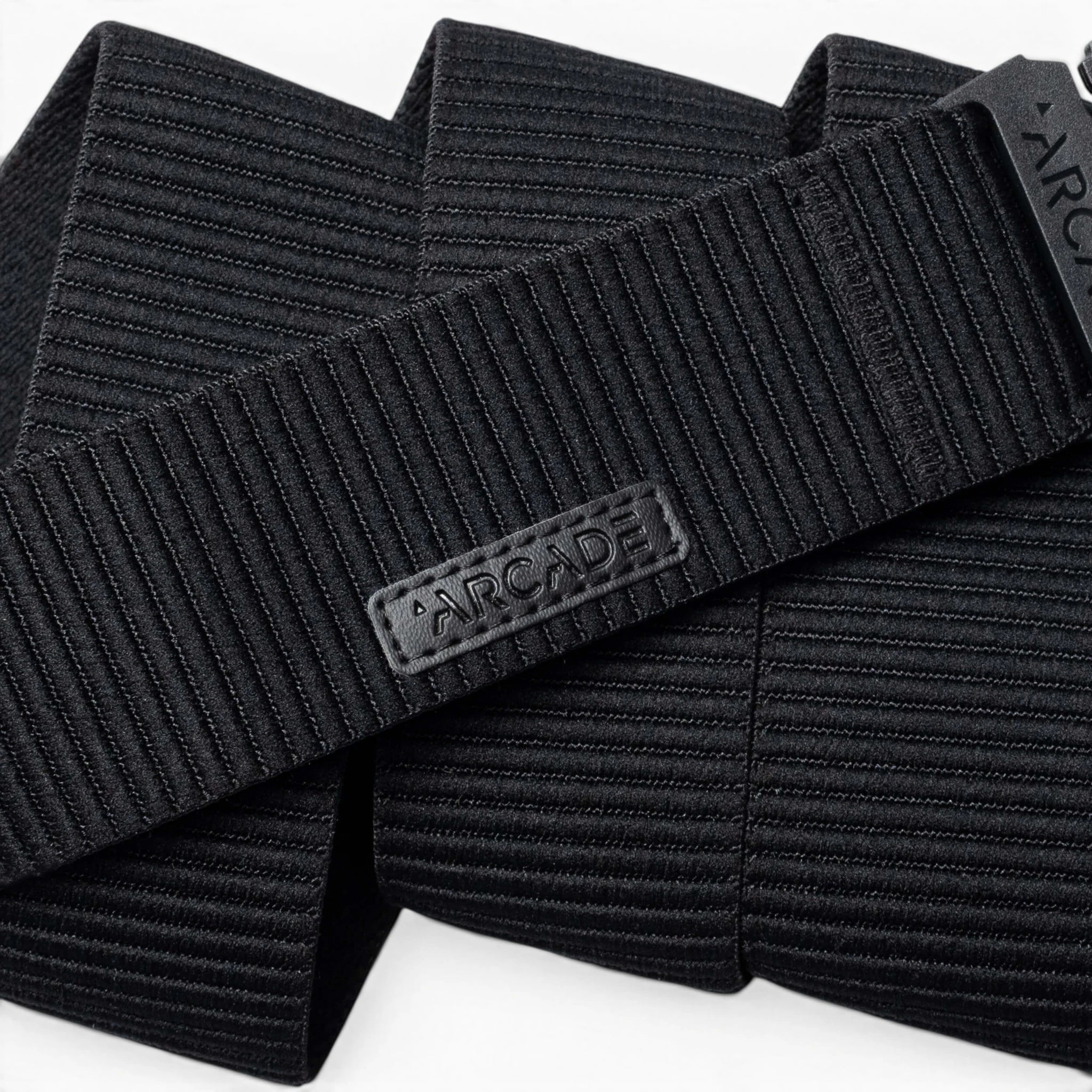 A close-up of the black, ribbed woven Woody belt by Arcade Belts features a rectangular patch with ARCADE in raised letters, showcasing its durable stitching and elastic stretch design.