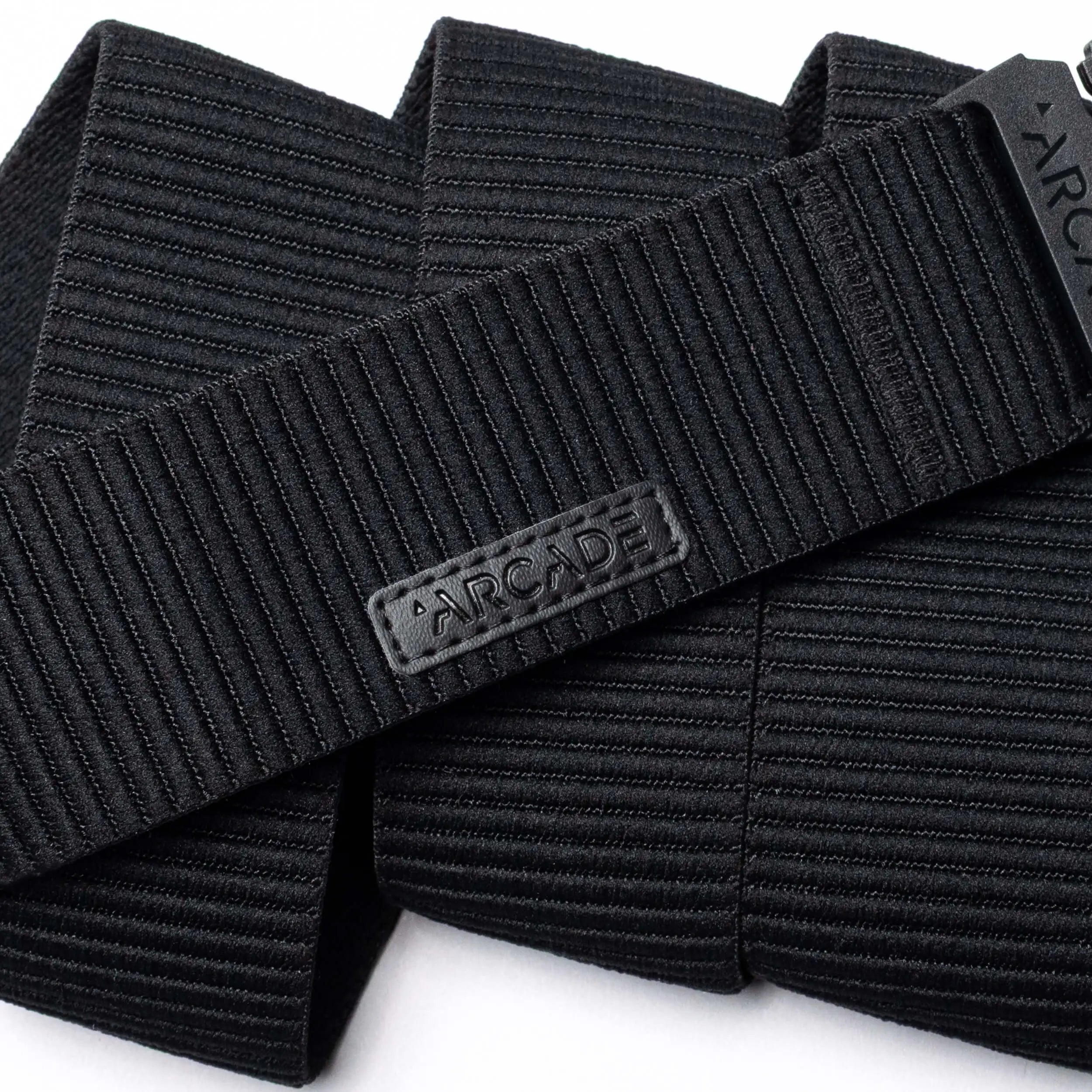 A close-up of the black, ribbed woven Woody belt by Arcade Belts features a rectangular patch with ARCADE in raised letters, showcasing its durable stitching and elastic stretch design.