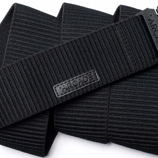 A close-up of the black, ribbed woven Woody belt by Arcade Belts features a rectangular patch with ARCADE in raised letters, showcasing its durable stitching and elastic stretch design.