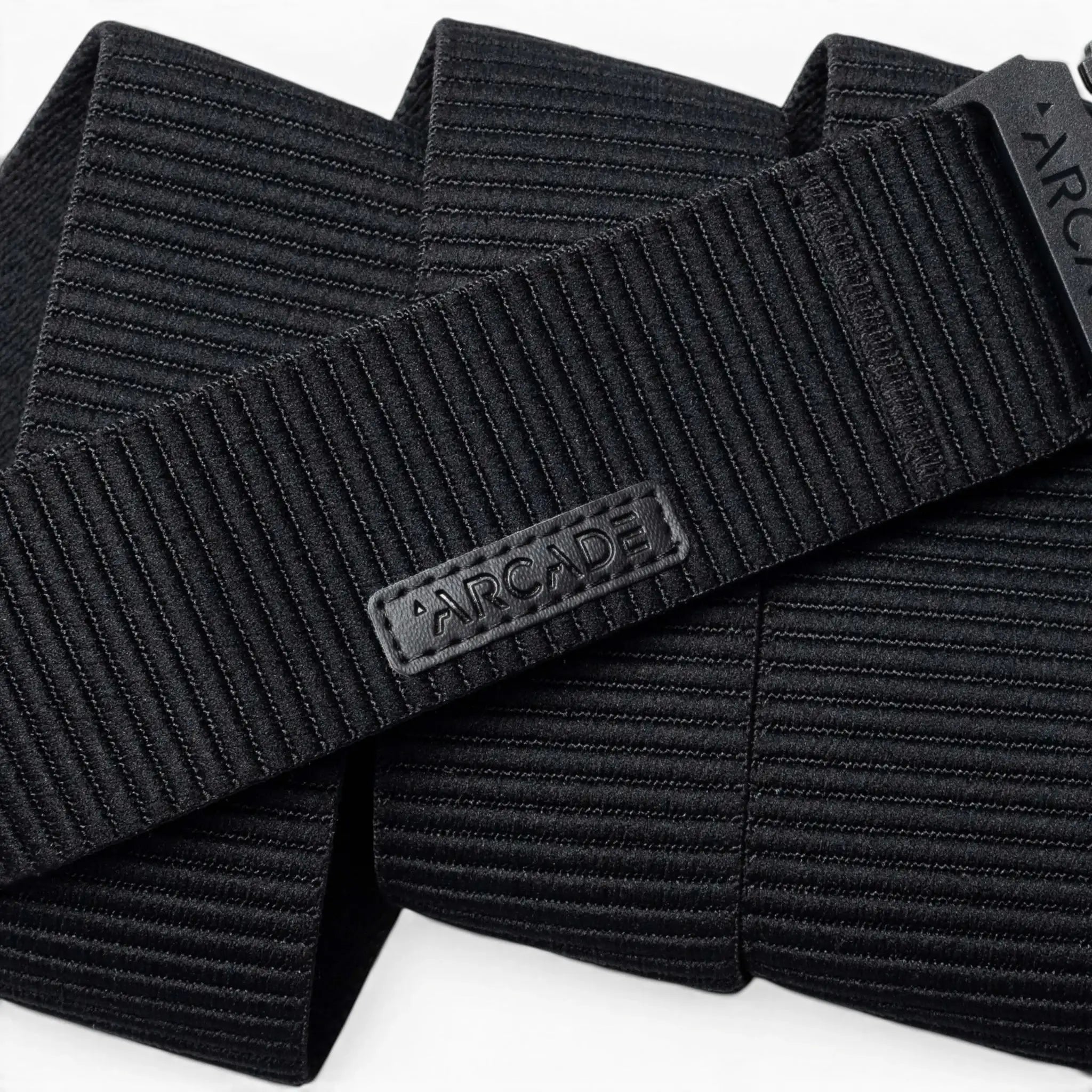 A close-up of the black, ribbed woven Woody belt by Arcade Belts features a rectangular patch with ARCADE in raised letters, showcasing its durable stitching and elastic stretch design.