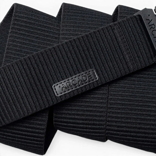 A close-up of the black, ribbed woven Woody belt by Arcade Belts features a rectangular patch with ARCADE in raised letters, showcasing its durable stitching and elastic stretch design.