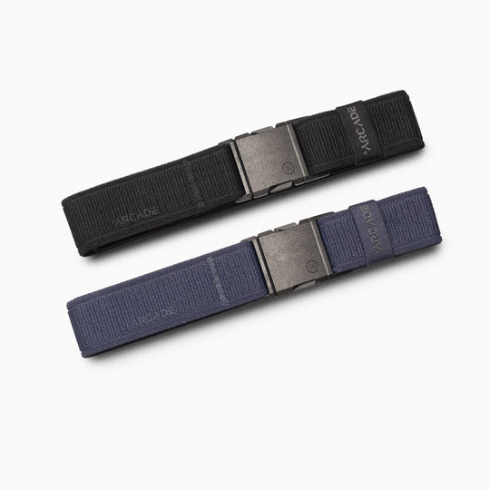 The Arcade Belts A2 Youth Kit includes two stretch webbing belts, one black and one navy blue, each with a matte rectangular metal buckle, laid flat and parallel on a white background for signature comfort.