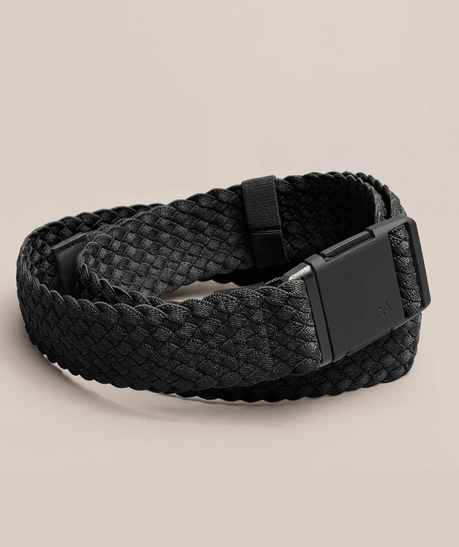 A black braided belt with a matte black rectangular buckle, neatly coiled on a light beige surface.
